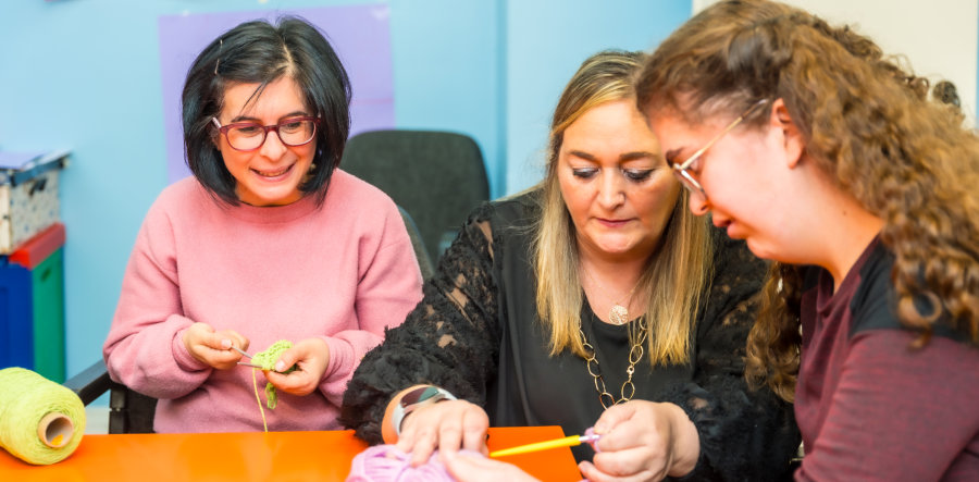 three women crafting with colorful yarn indoors